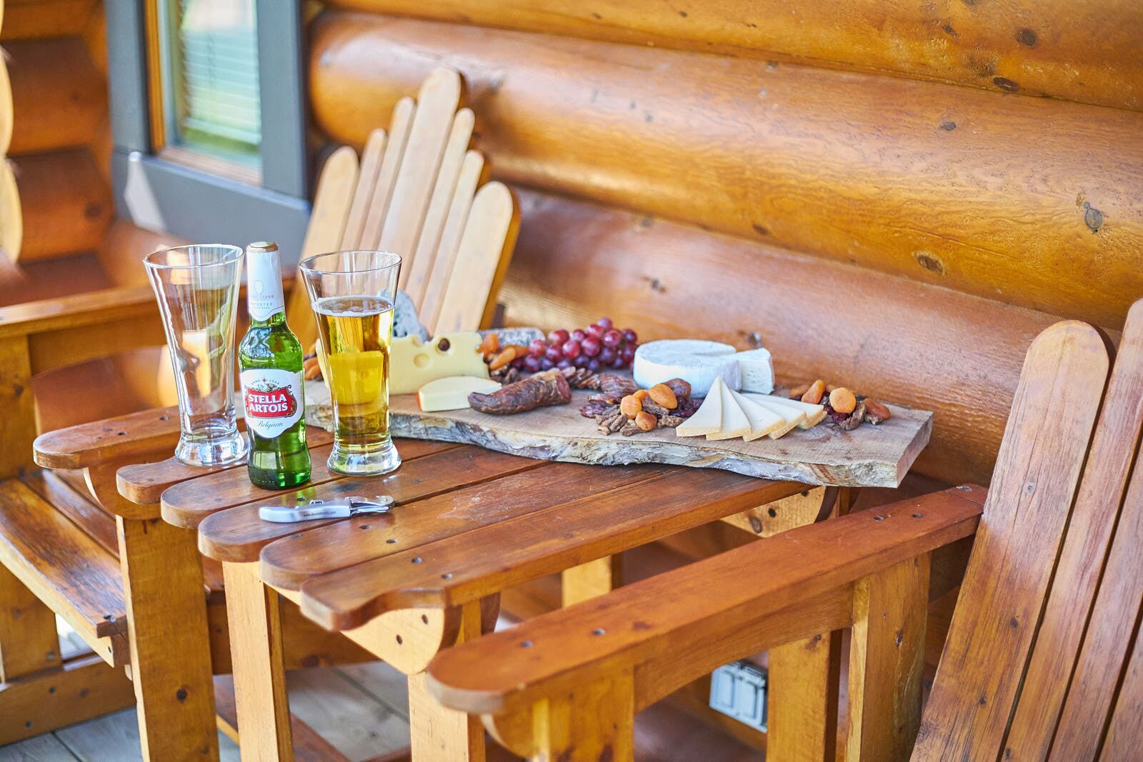 Un banco de madera con una tabla de quesos, vasos y una botella de cerveza.
