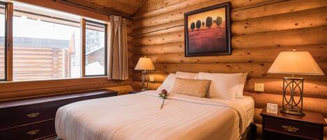 Un dormitorio de estilo cabaña de madera con una cama grande, dos mesitas de noche con lámparas, una ventana con cortinas y un cuadro en la pared.