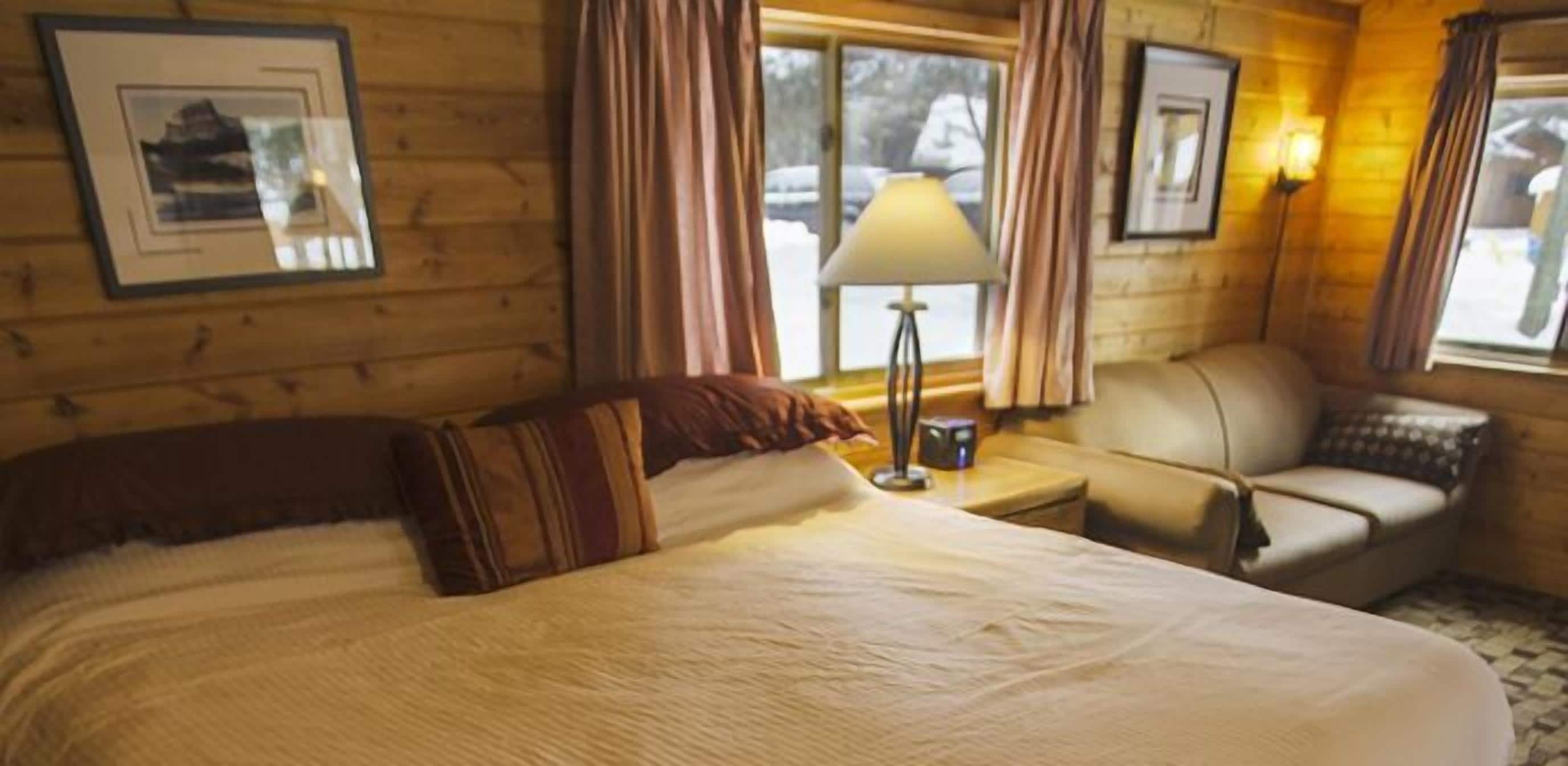 A cozy room with a large bed, a small sofa, a lamp, and framed pictures on the walls.