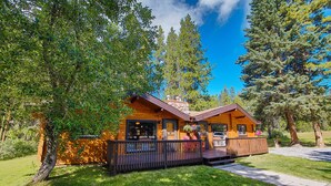 A wooden cabin with a porch, surrounded by trees and a clear sky. - Castle Mountain Chalets (Castle Junction)
