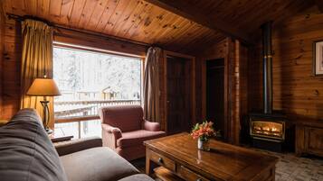 Un acogedor interior de cabaña con un sofá, una mesa de madera, una chimenea y una ventana con cortinas.