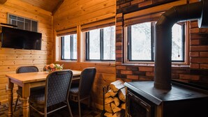 A wooden cabin interior with a dining table, chairs, a fireplace, and a television mounted on the wall. - Castle Mountain Chalets (Castle Junction)