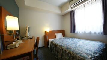 Una habitación de hotel con cama, escritorio, silla, lámpara y aire acondicionado.