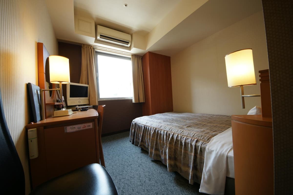 A hotel room with a bed, a desk with a computer, a chair, and a lamp.