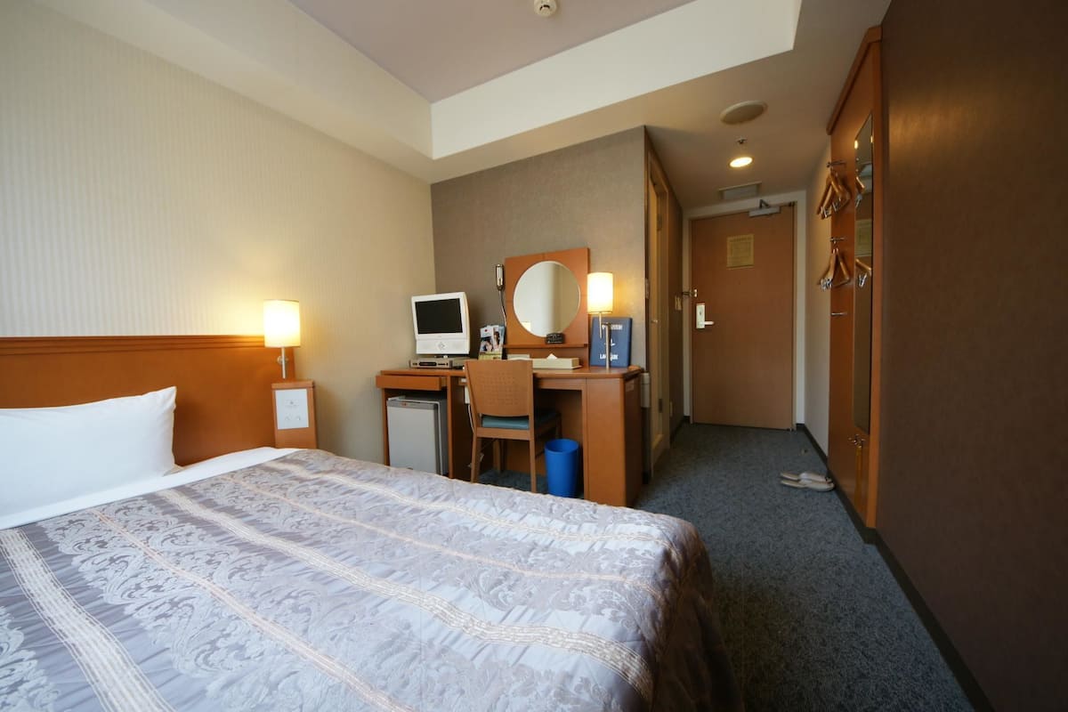 A hotel room with a bed, desk, chair, and a mirror.