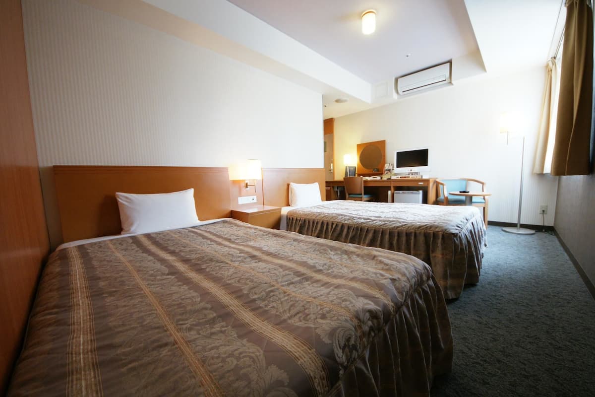 A hotel room with two beds, a desk, a chair, a television, and a window with curtains.
