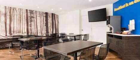 A modern conference room with a large table, chairs, a TV, and a wall with a forest mural.