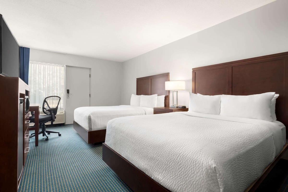 A hotel room with two beds, a desk, and a chair.