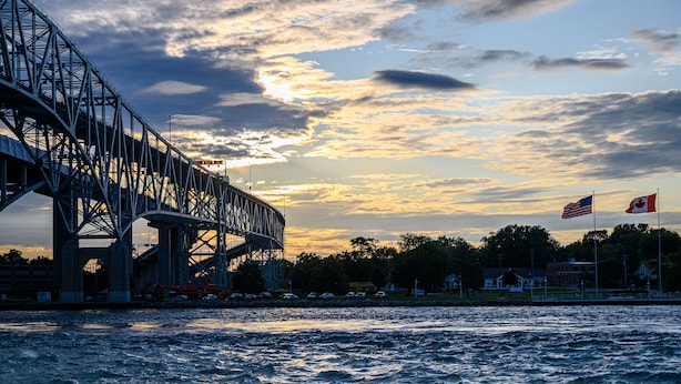 Un pont orné de deux drapeaux, un américain et un canadien, se dressant sur fond de ciel au coucher du soleil.