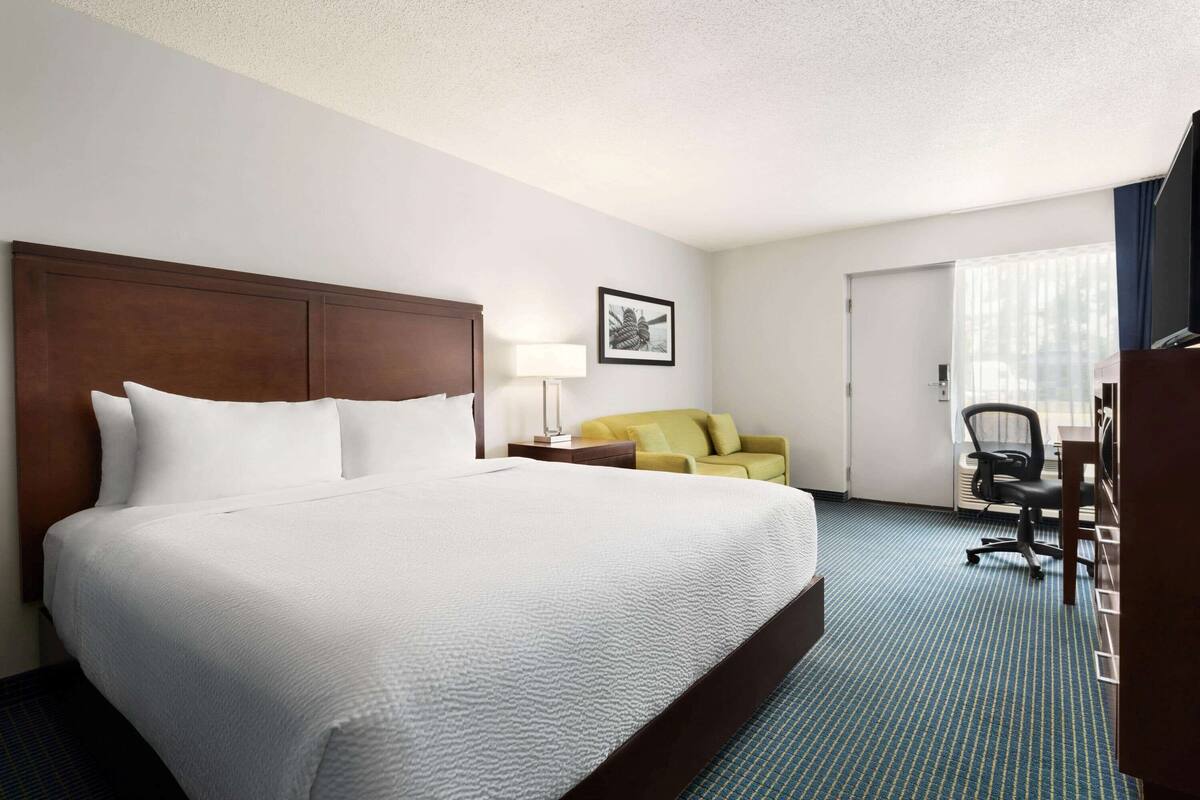 A hotel room with a large bed, a desk, a chair, a sofa, and a window with curtains.