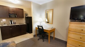 Kompakti hotellihuone, jossa on pieni keittiönurkkaus, työpöytä tuolilla, televisio ja puinen lipasto.