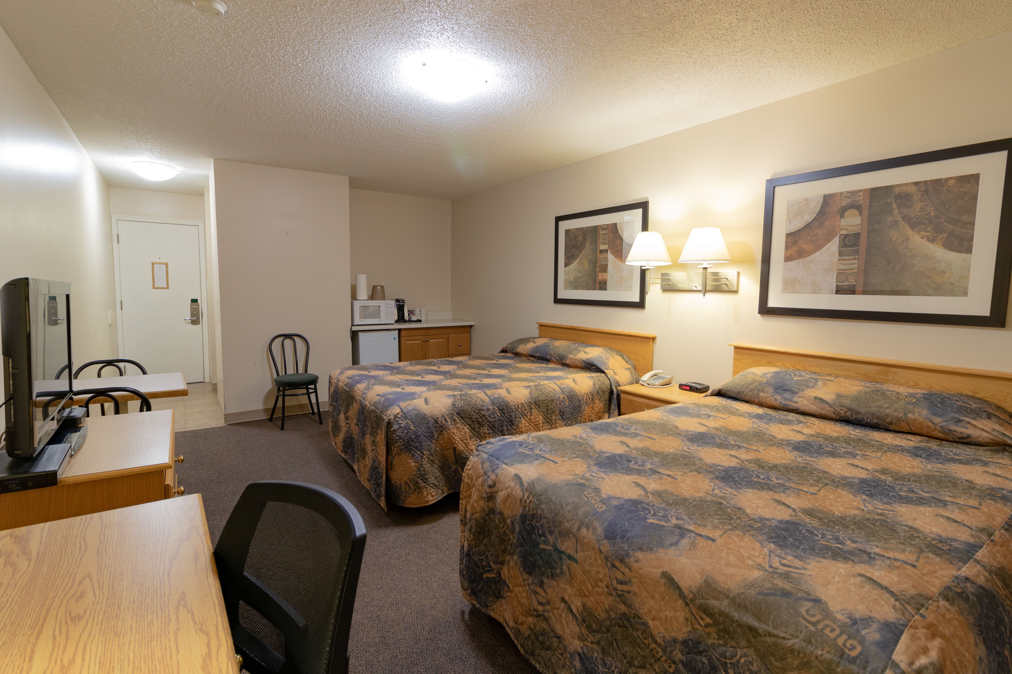 A hotel room with two beds, a desk, a chair, a television, and a microwave.