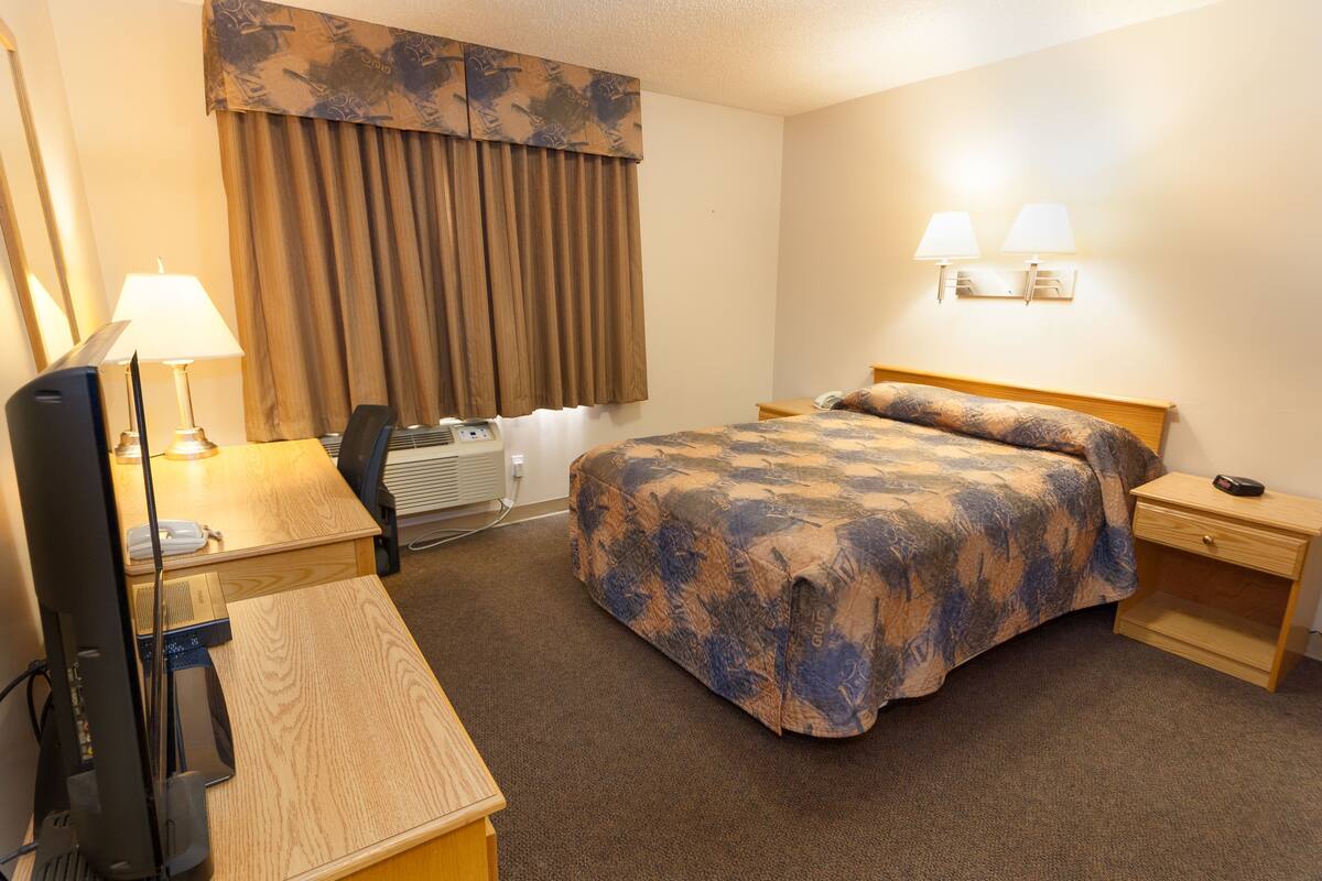A hotel room with a bed, desk, chair, lamp, and a telephone.