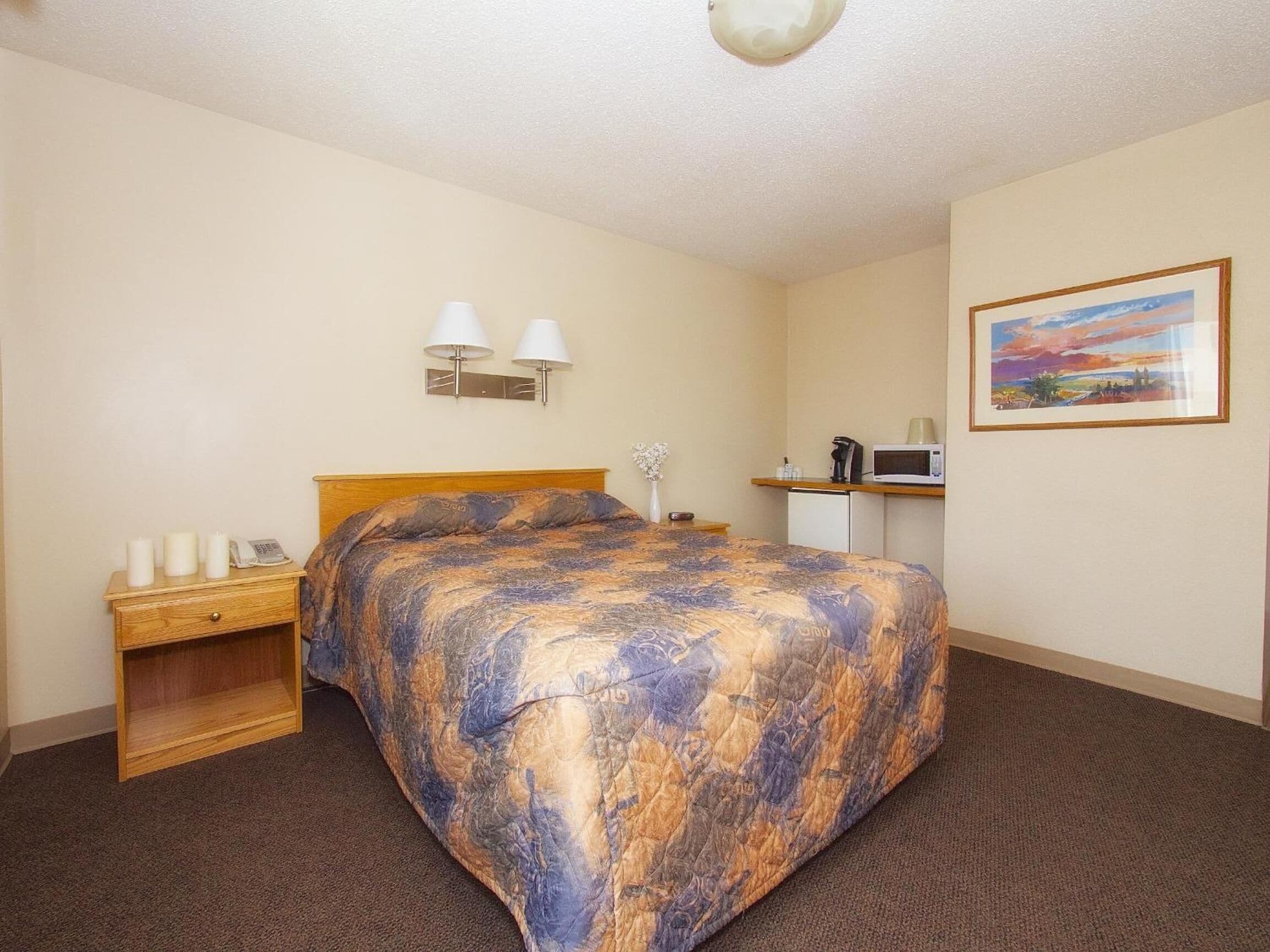 Una habitación de hotel con cama, mesita de noche, lámpara y un cuadro en la pared.