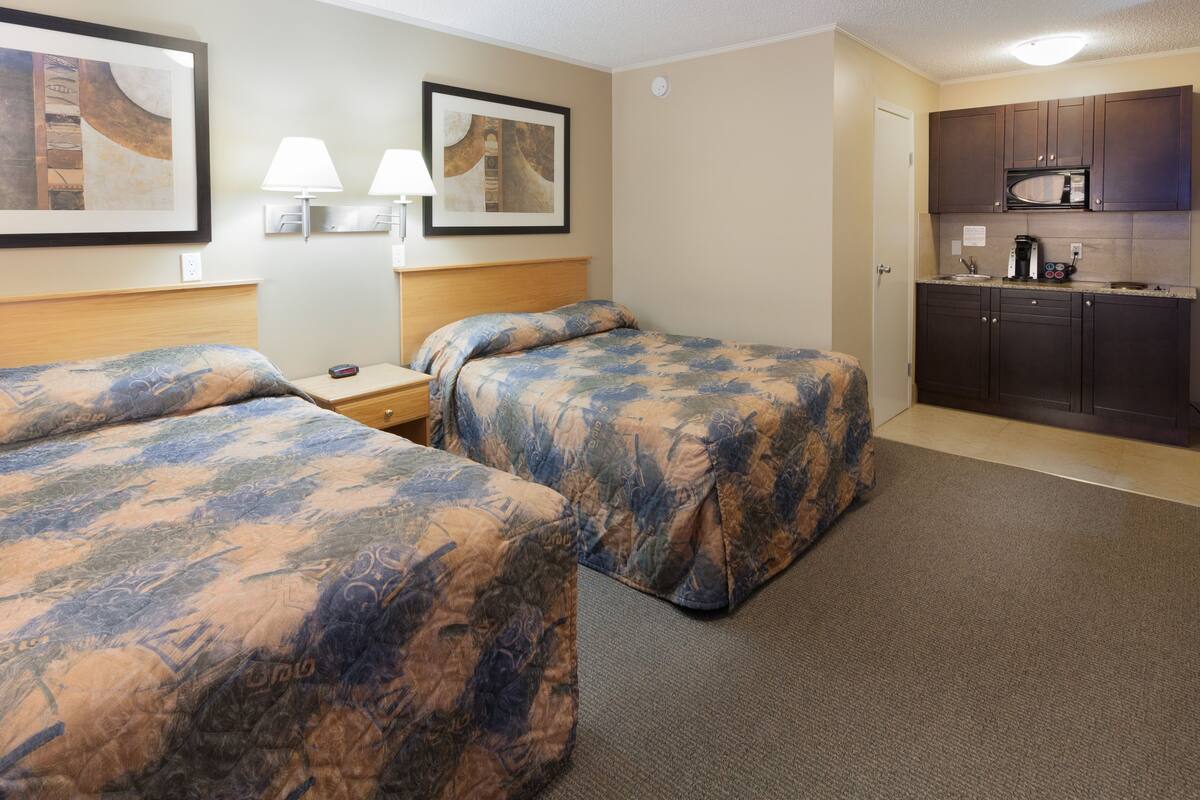 A hotel room with two beds, a small desk, a nightstand, a microwave, and a coffee maker.