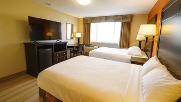 A hotel room with two beds, a TV, a desk, and a window with curtains.