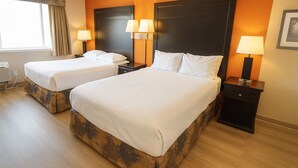Hotellihuone, jossa on kaksi sänkyä, suuri ikkuna, jossa on verhot, ja seinään kiinnitetty valaisin.