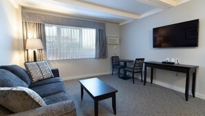 A modern hotel room with a sofa, a small table, a TV, and a window with curtains. - BCMInns Fort McMurray (Fort McMurray)