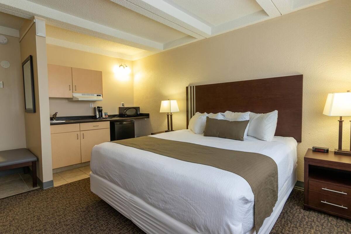 Habitación de hotel con cama, mesitas de noche, escritorio, microondas, cafetera y pequeña cocina.