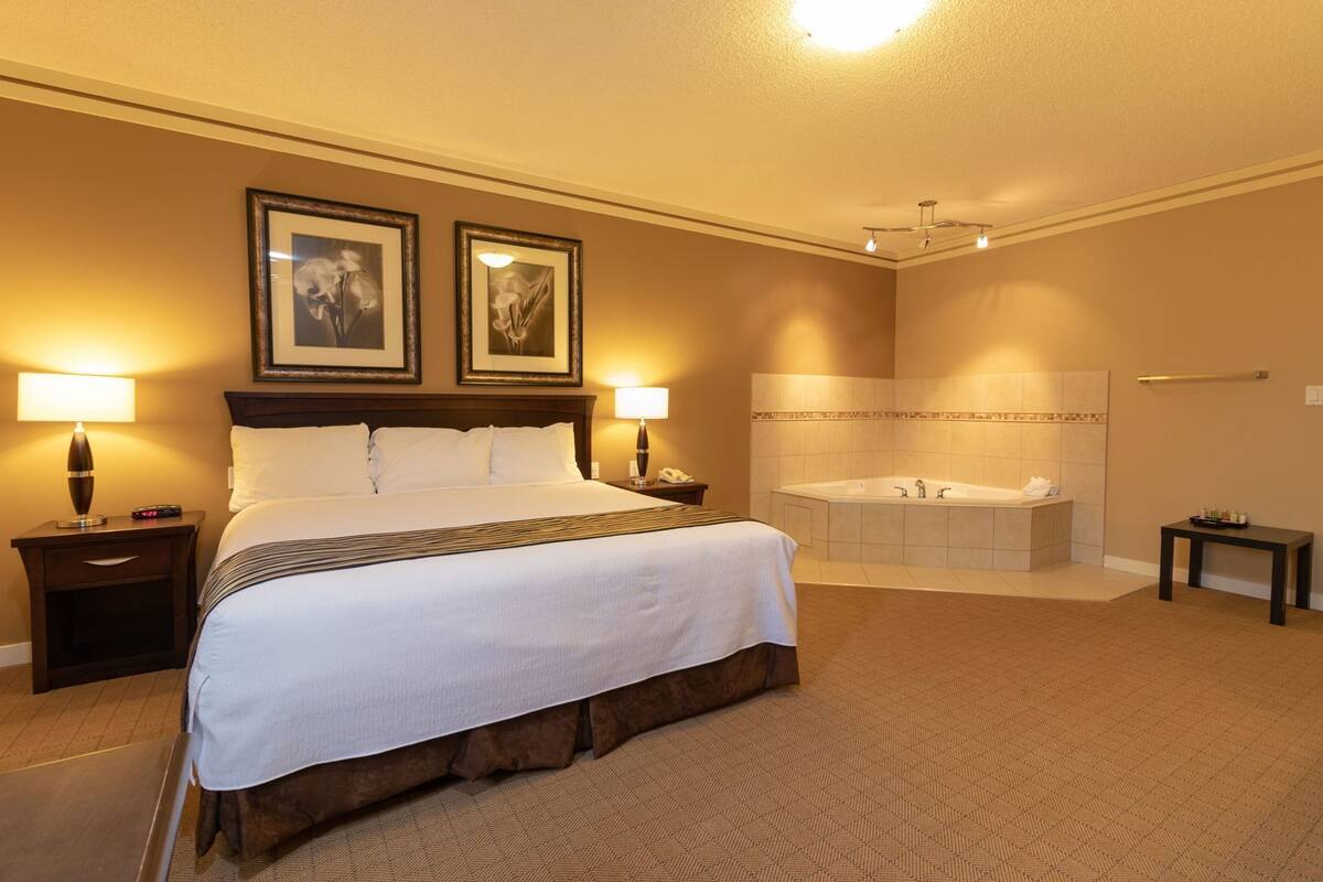 A hotel room with a large bed, a bathroom with a bathtub, and two framed pictures on the wall.