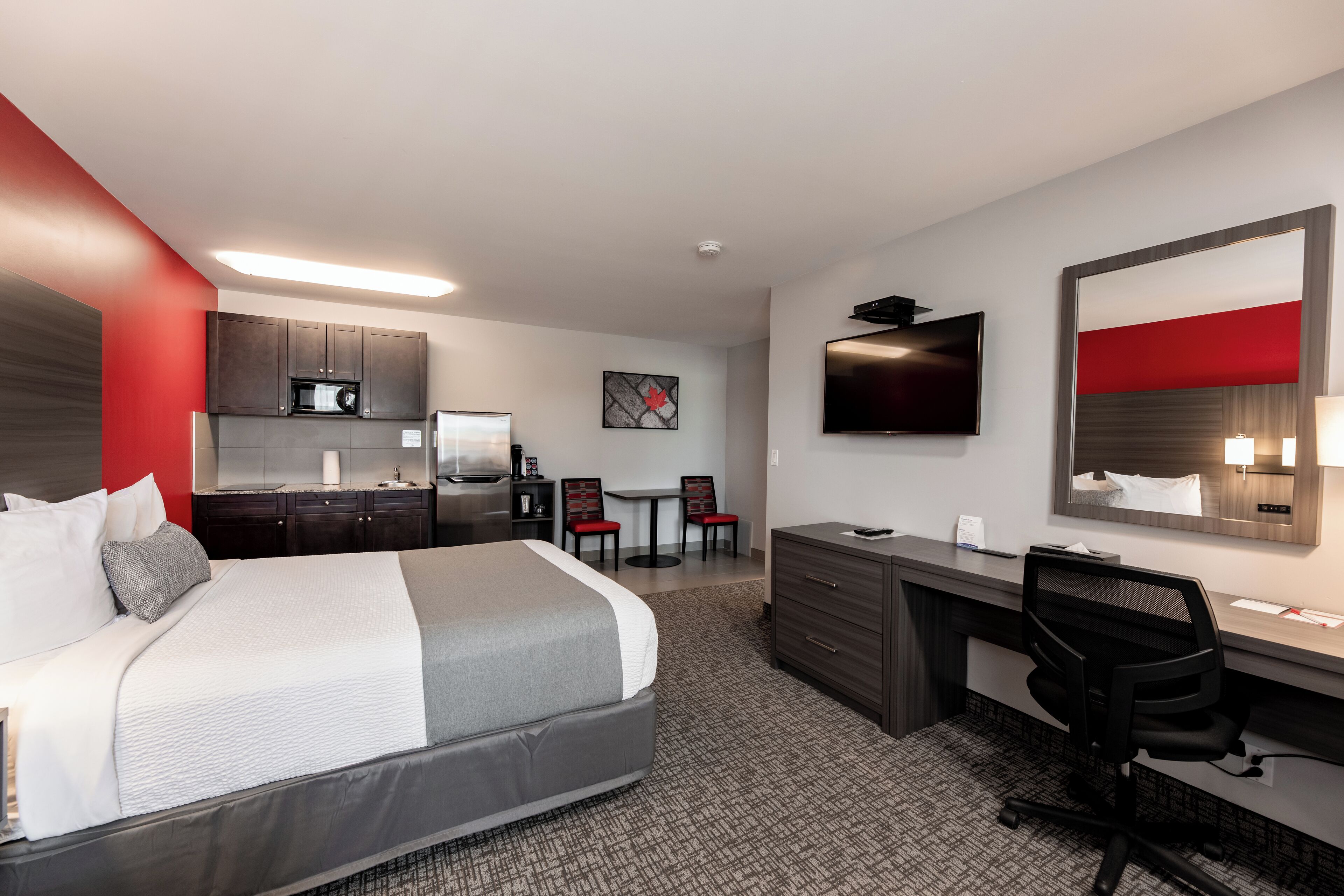 Habitación de hotel con cama, escritorio, silla, televisor, microondas y una pequeña cocina.