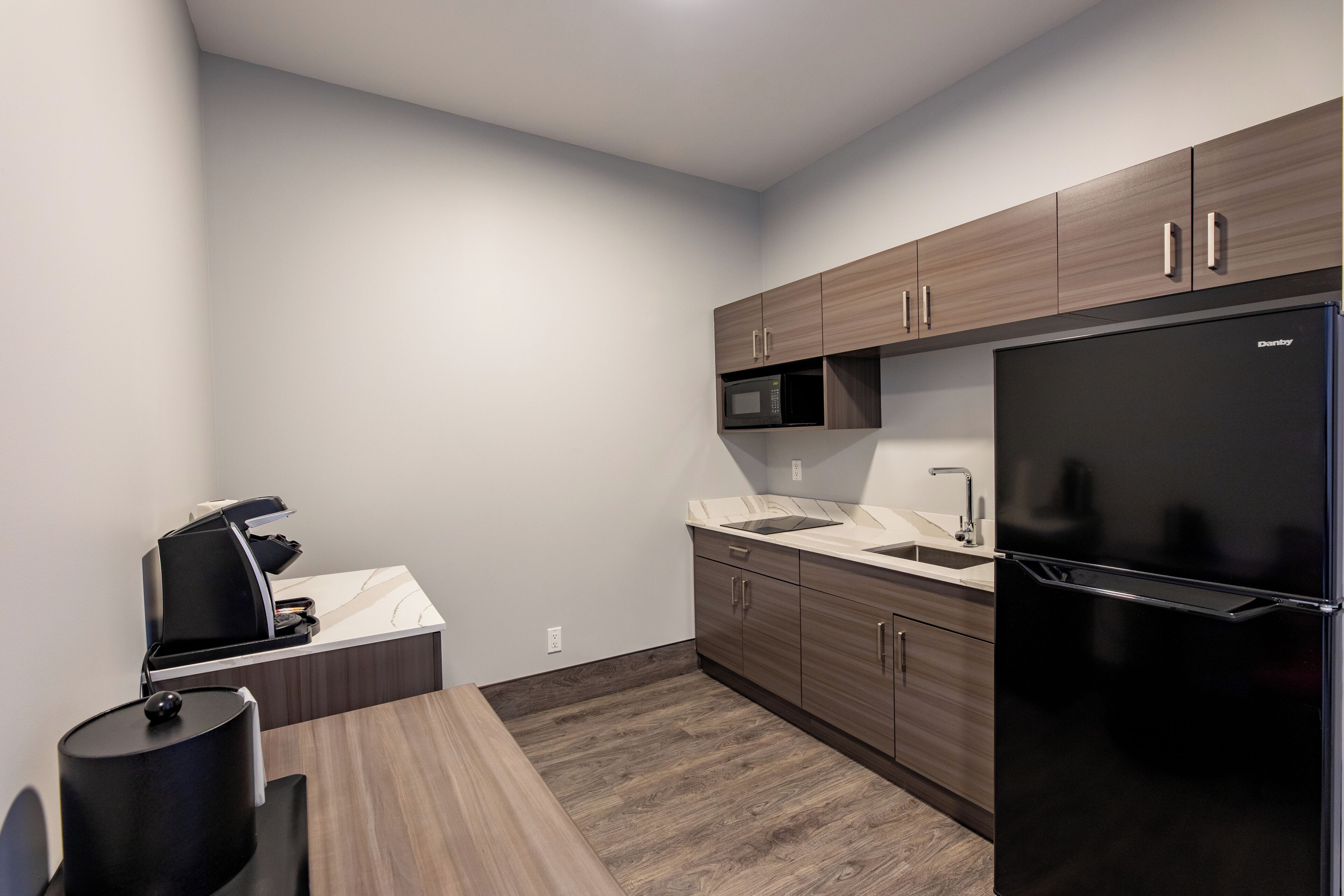A modern kitchen with a built-in microwave, a refrigerator, and a coffee machine.