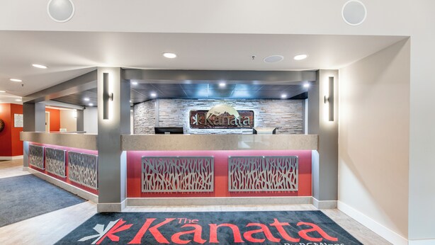 Ein Empfangsbereich im modernen Stil, mit einer Rezeption, einem Logo an der Wand und einem Teppich mit dem Namen des Hotels.