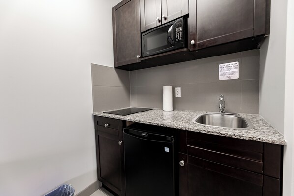 A compact kitchen with dark wood cabinets, a stainless steel sink, a microwave, and a dishwasher.