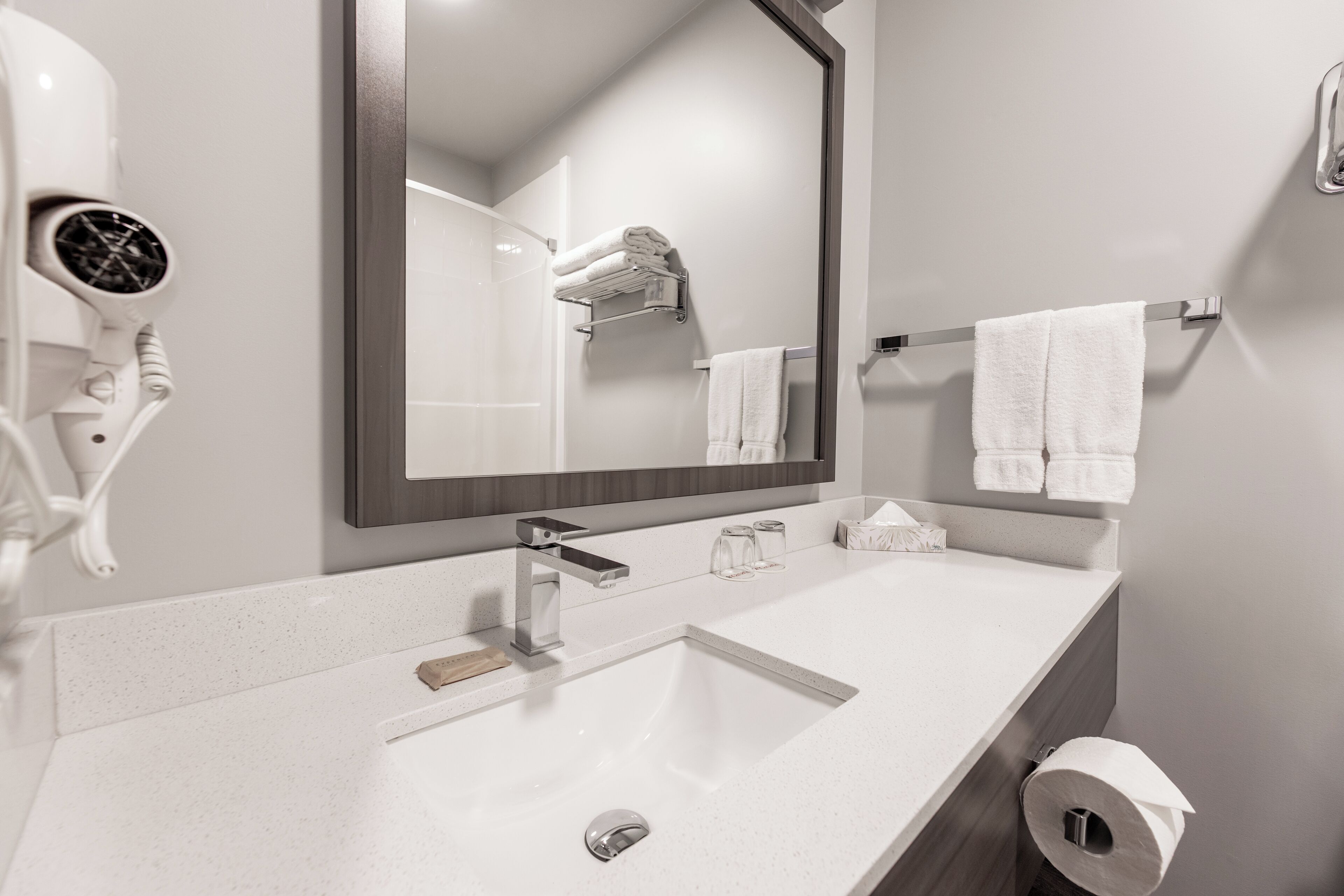 A modern bathroom with a white sink, a large mirror, a hairdryer, and neatly arranged towels.