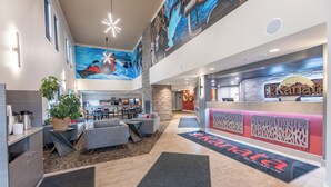 Eine moderne Hotelhalle mit hoher Decke, einer zentralen Sitzecke, einer Rezeption und einem Wandgemälde.