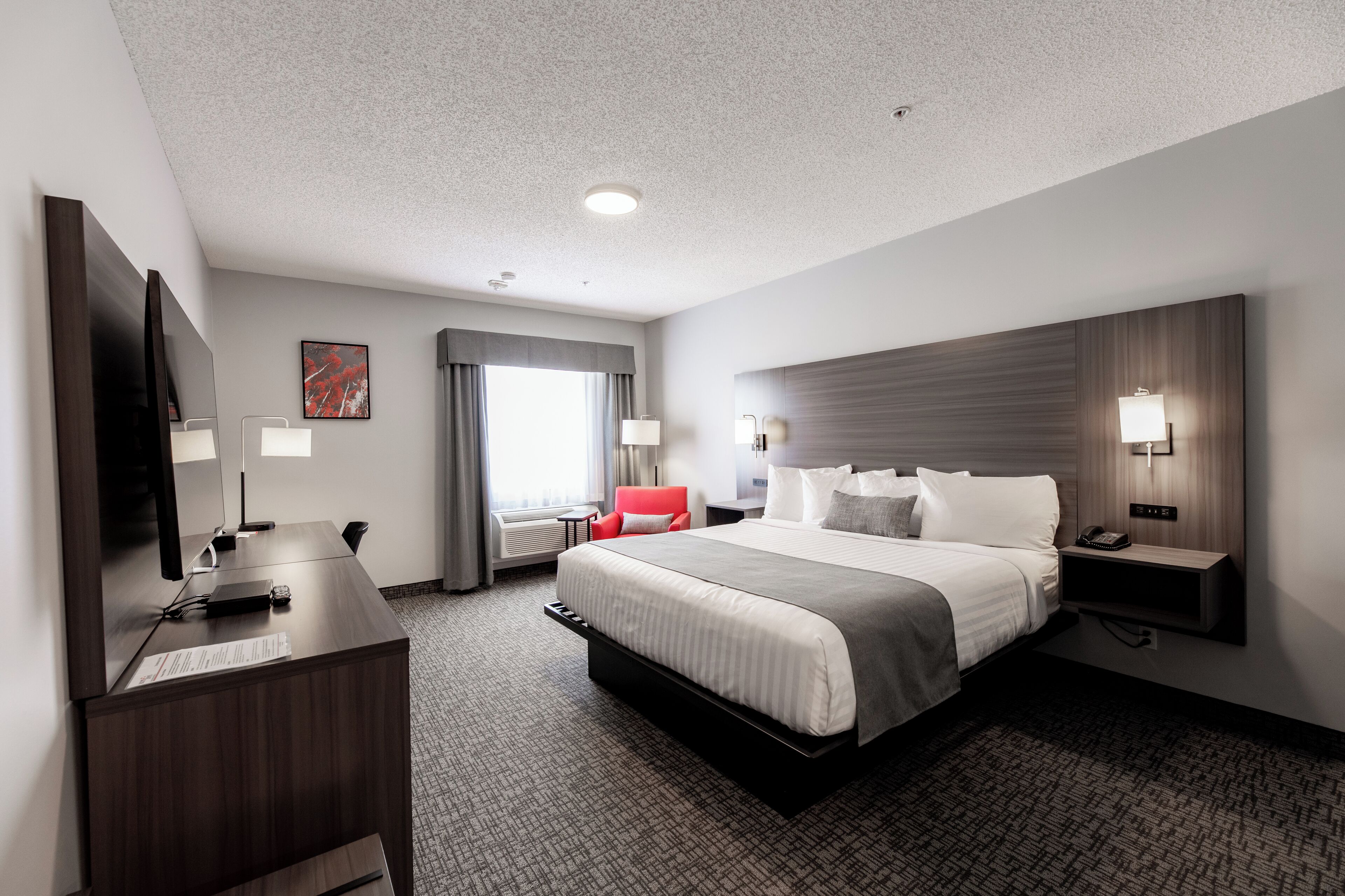 Habitación de hotel moderna con una cama grande, un escritorio con computadora, una silla roja y un televisor.