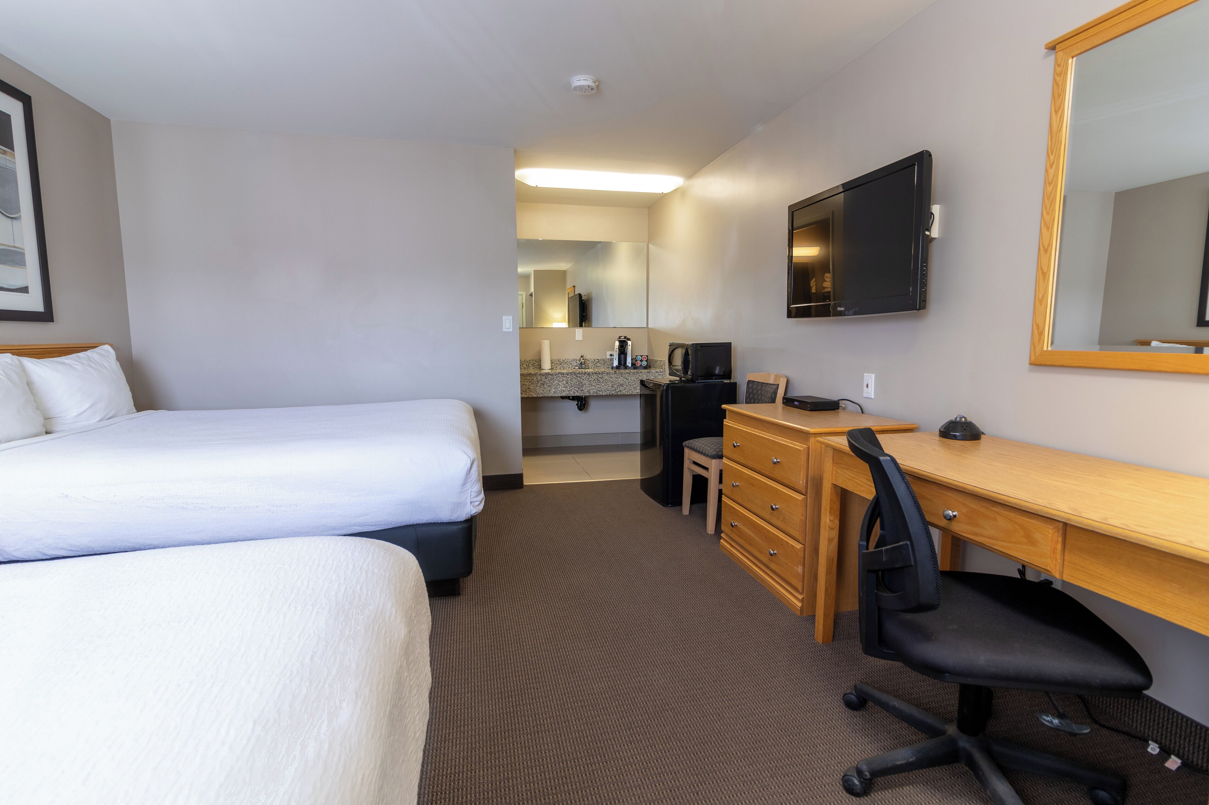 Quarto de hotel com duas camas, uma escrivaninha com cadeira, televisão e espelho.