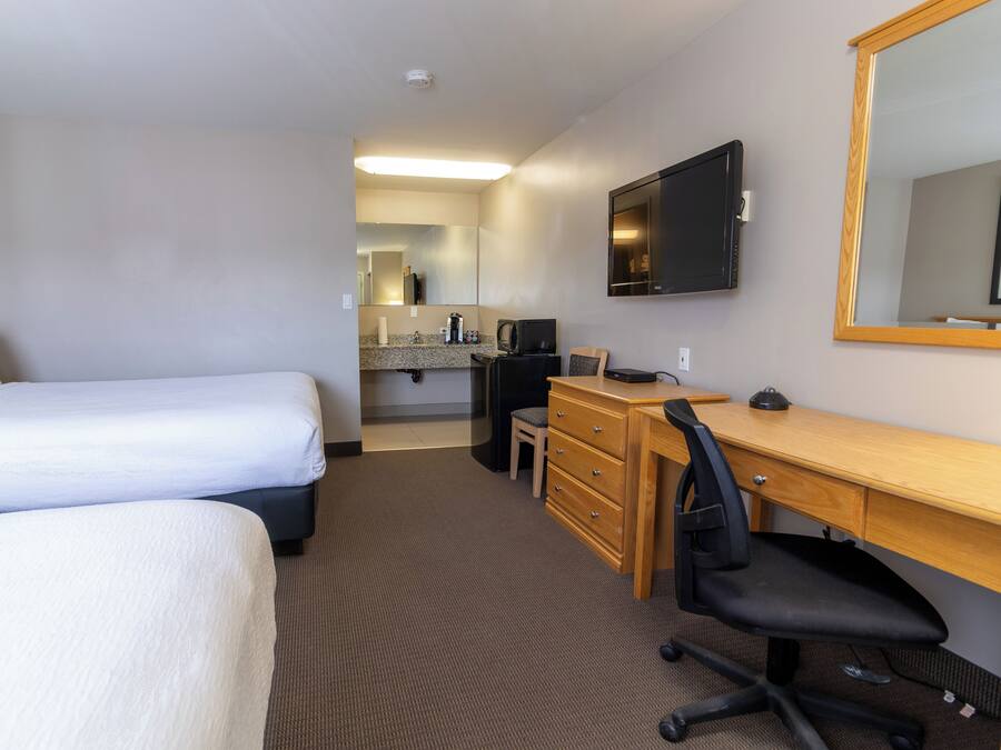 Quarto de hotel com duas camas, uma escrivaninha com cadeira, televisão e espelho.