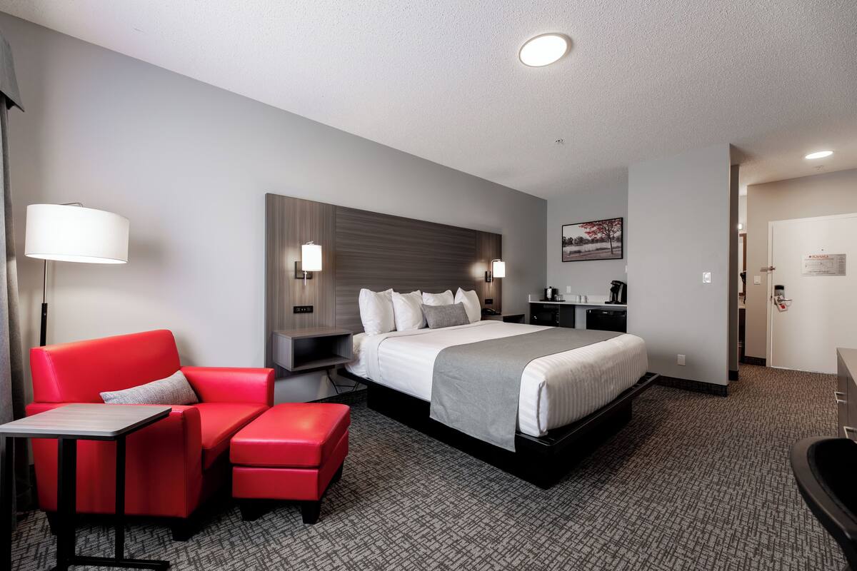 A hotel room with a bed, a red sofa, a small table, a desk, and a lamp.