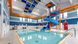 Ein Innenpool mit einer blauen Rutsche, gelben Sicherheitshinweisen und einer roten Notausgangstür.