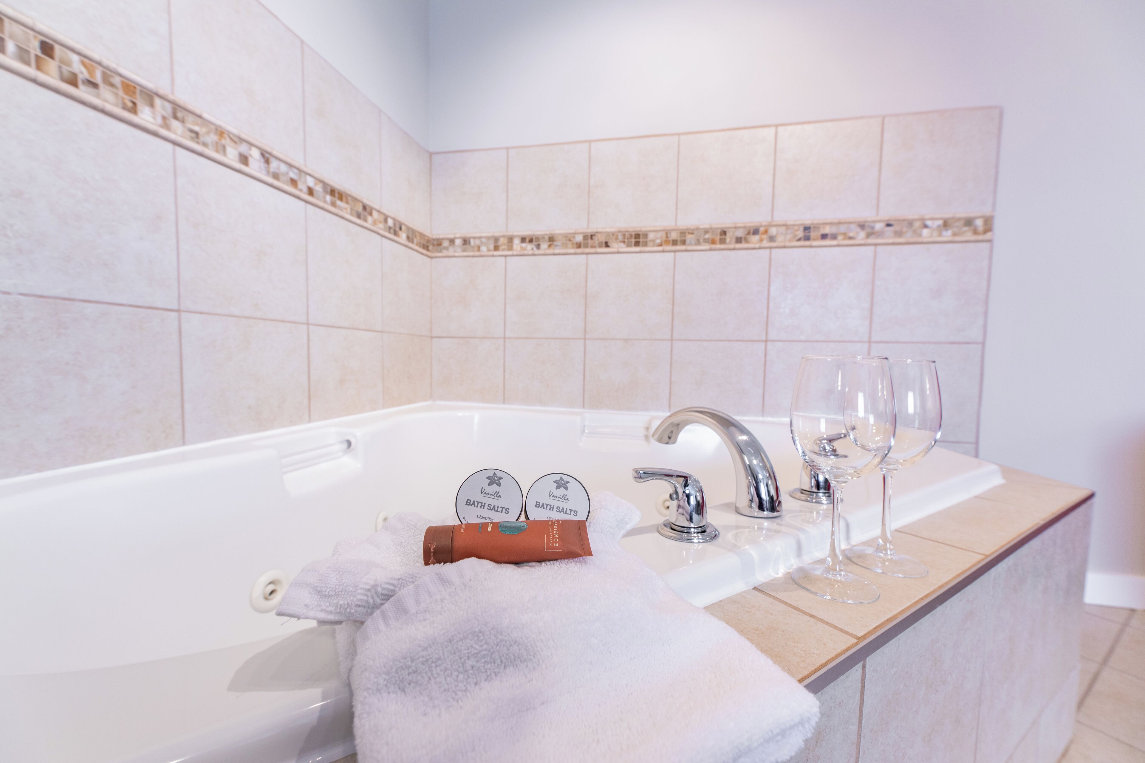 Un baño con bañera, lavamanos y dos copas de vino sobre el mostrador.