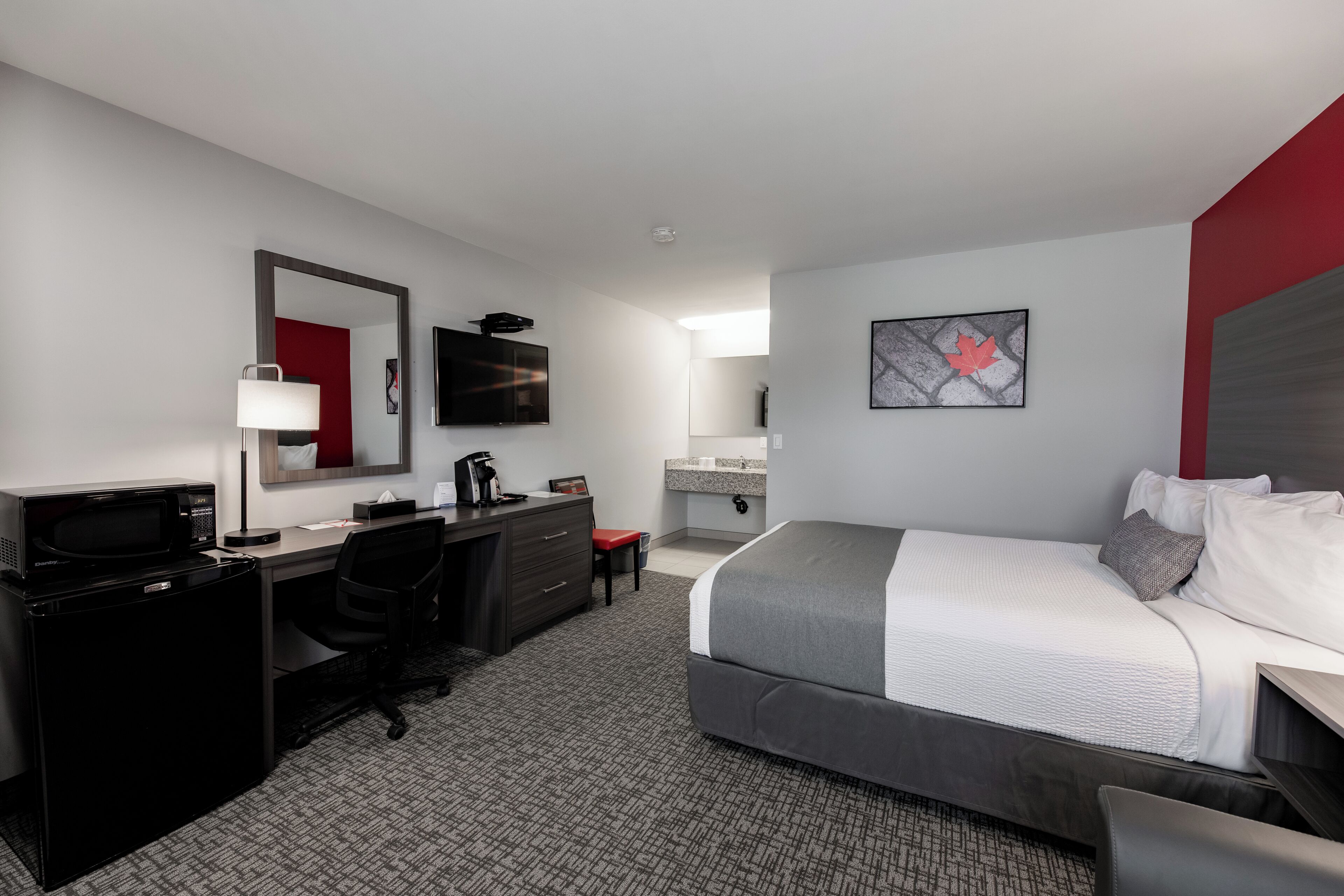 A modern hotel room with a bed, desk, and a small kitchenette.