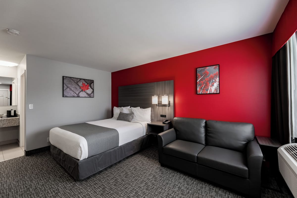 A hotel room with a bed, a sofa, a nightstand, and artwork on the walls.