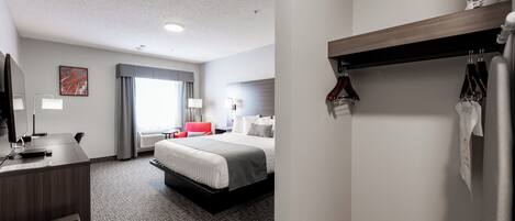 A hotel room with a bed, desk, and a hanging coat rack.