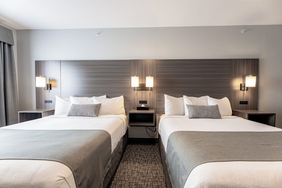 A hotel room with two beds, a nightstand with a lamp, and a wall-mounted light fixture.