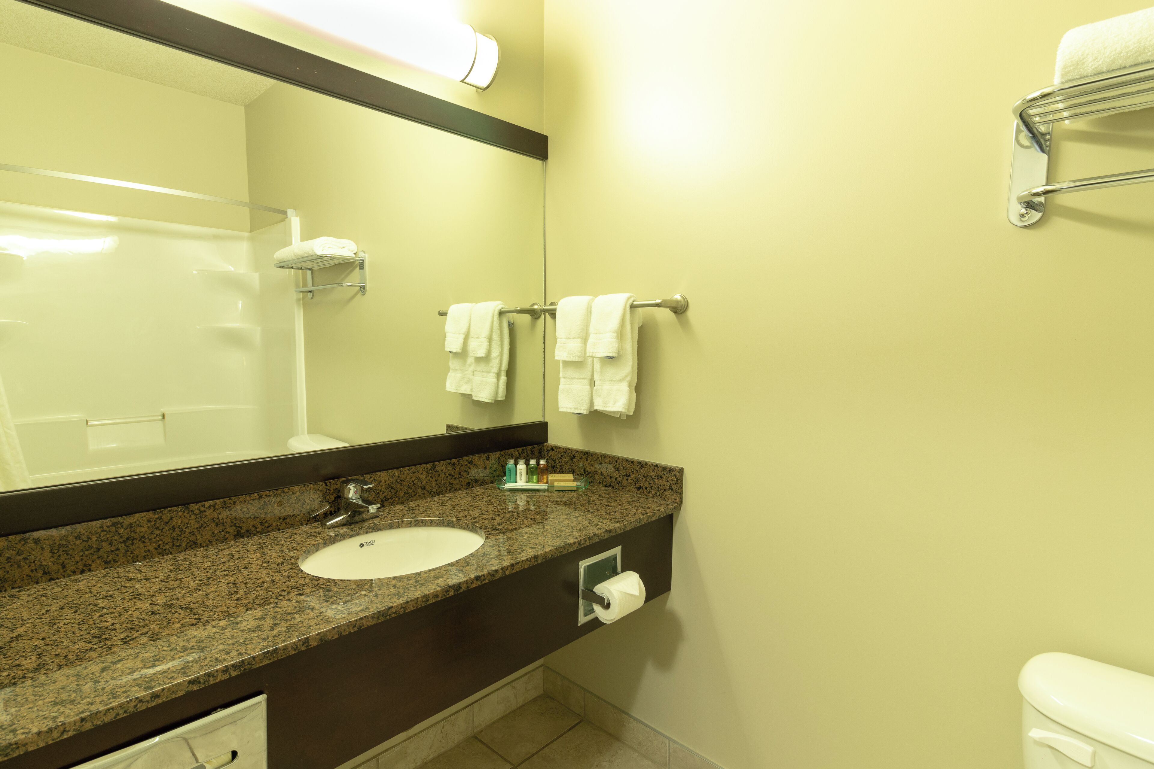 A bathroom with a granite countertop, a white sink, a mirror, a towel rack, and a toilet.