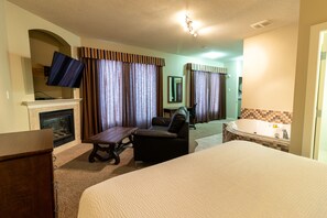 A hotel room with a large bed, a desk, a chair, a fireplace, a television, and a bathtub. - BCMInns Lac La Biche (Lac La Biche)
