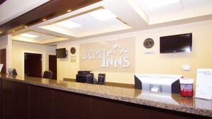 A hotel reception area with a reception desk, a clock, a television, and a sign for BCM Inns. - BCMInns Lac La Biche (Lac La Biche)