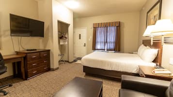 Una habitación de hotel con cama, escritorio, silla, televisor, lámpara y perchero.