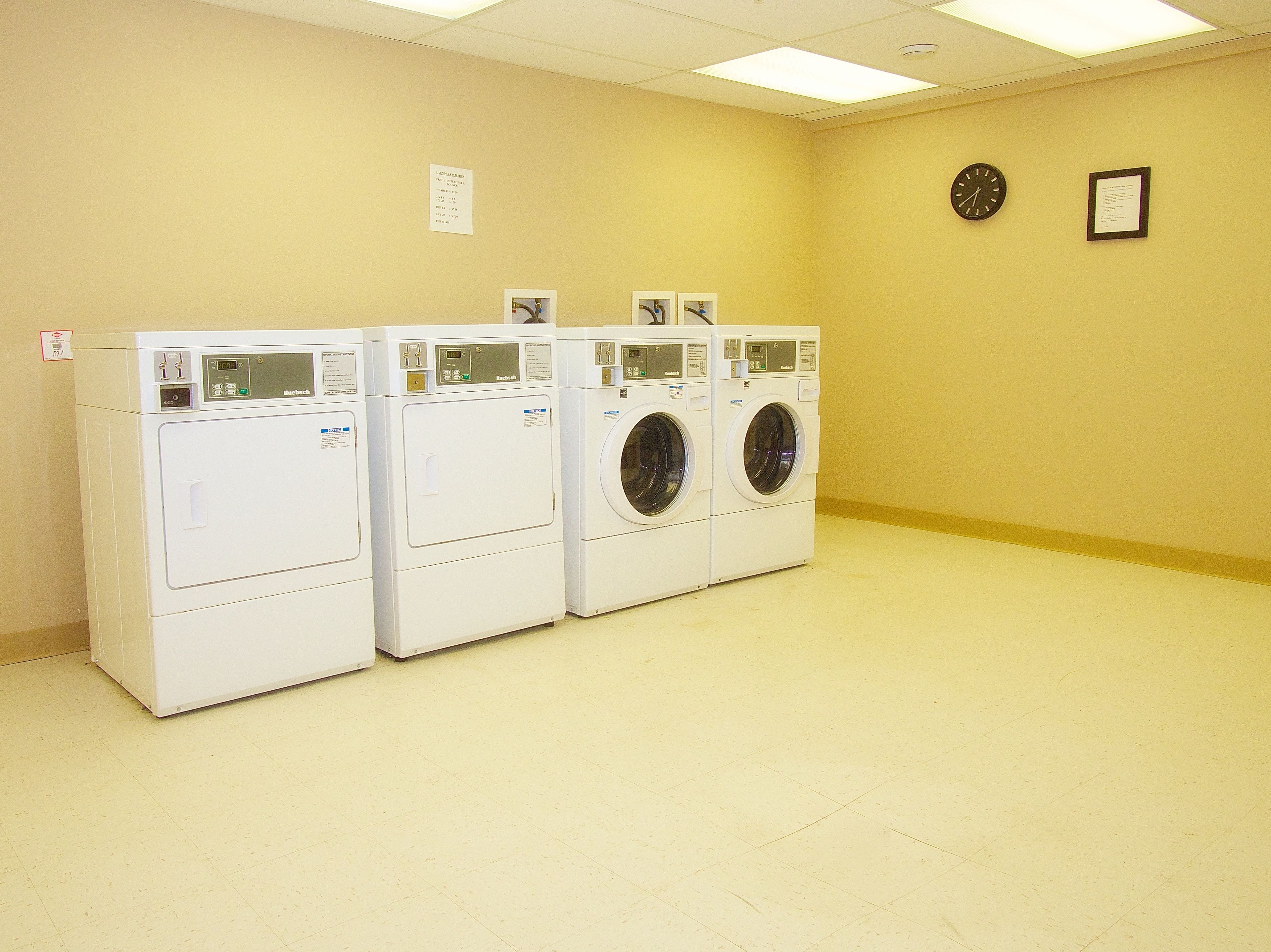 A row of three white front-loading washing machines in a room with yellow walls and a tiled floor.