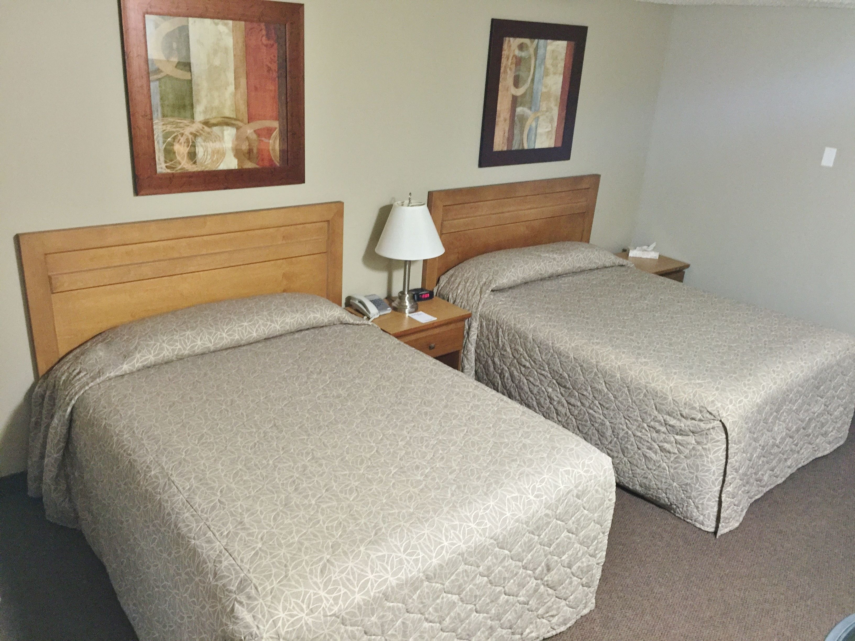A hotel room with two beds, a nightstand with a lamp, and two framed artworks on the wall.