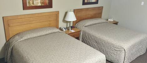A hotel room with two beds, a nightstand with a lamp, and two framed artworks on the wall.