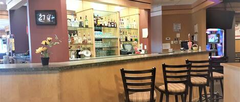 A bar area with a counter, shelves with bottles, and bar stools.