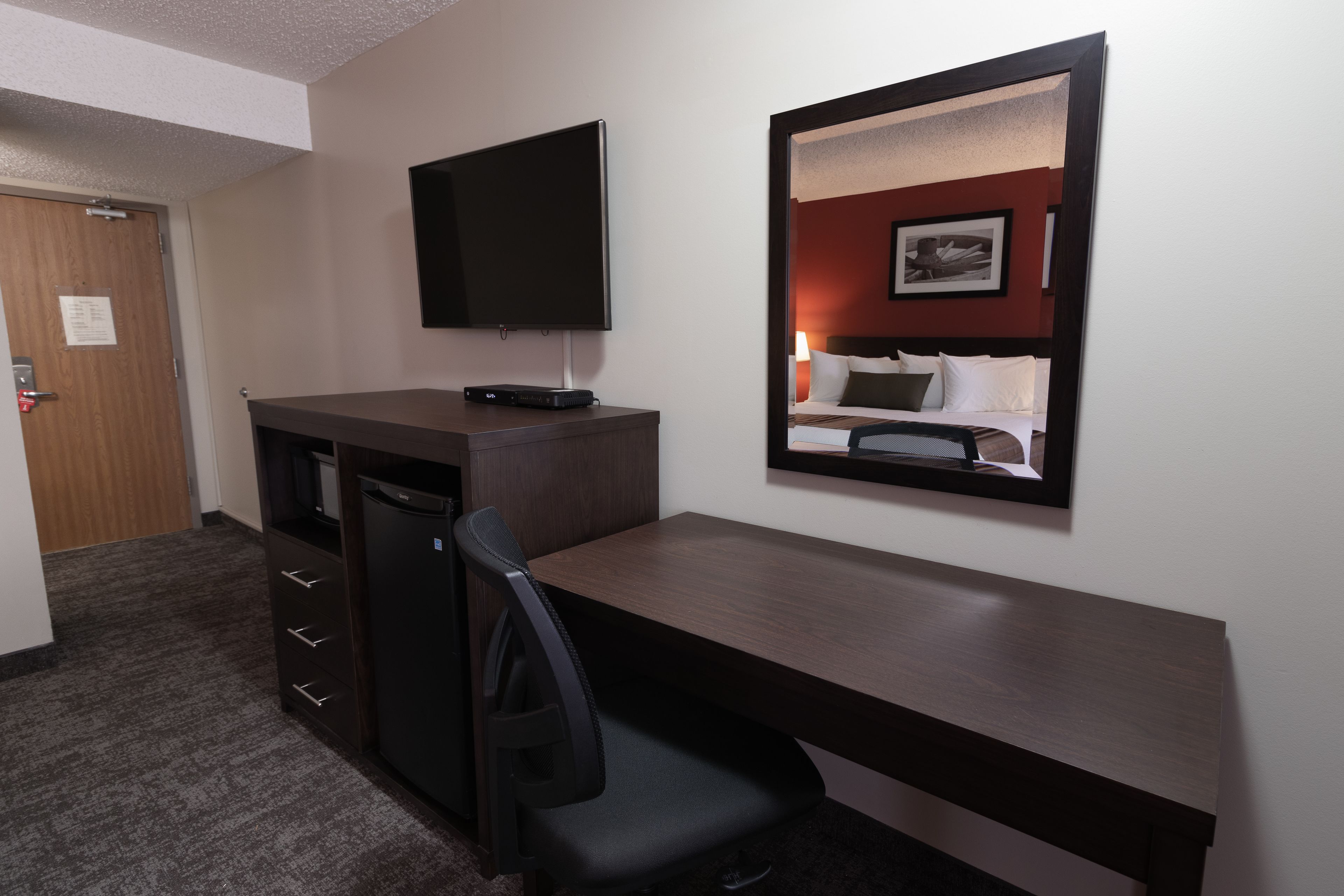 Een hotelkamer met een bureau, stoel, televisie en een bed met hoofdeinde.