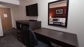 Een hotelkamer met een bureau, stoel, televisie en een bed met hoofdeinde.